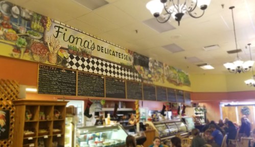 Interior of Fiona's Delicatessen featuring a colorful mural and menu board, with diners seated at tables.