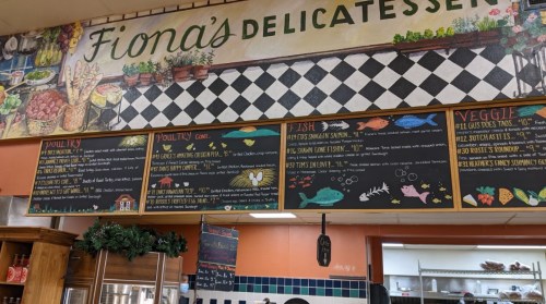 Menu board at Fiona's Delicatessen featuring poultry, fish, and veggie options with colorful illustrations.