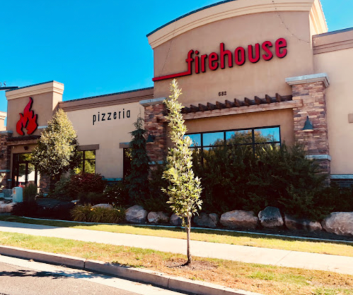 Exterior of a pizzeria named "Firehouse," featuring a stone facade and landscaping in front.