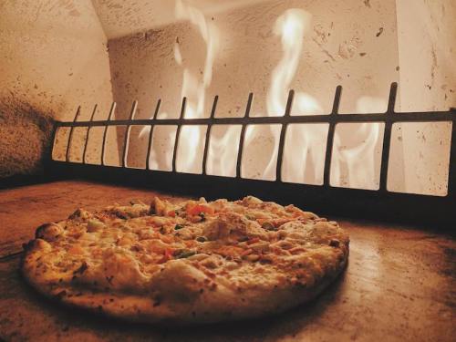 A freshly baked pizza sits on a stone surface in front of a roaring fire in a brick oven.