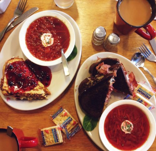 A table with two plates: one with soup and a sandwich, the other with toast topped with jam, and coffee mugs.