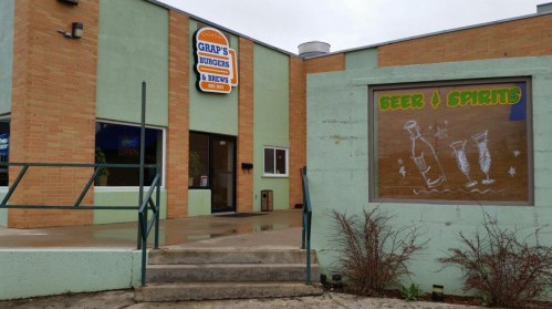Exterior of Grap's Bunches & Brews, featuring a sign and a window display for beer and spirits. Wet pavement visible.
