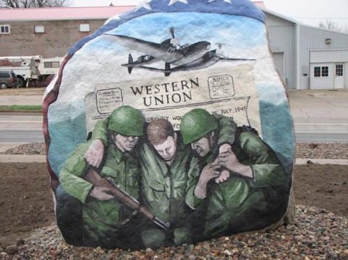 A painted rock depicting three soldiers reading a Western Union telegram, with a plane flying overhead.
