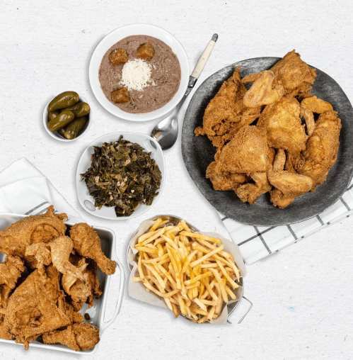A spread of fried chicken, collard greens, fries, black-eyed peas, and pickles on a textured background.