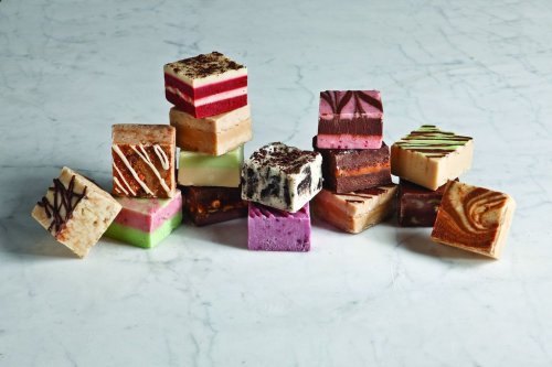 A colorful assortment of fudge squares stacked on a marble surface, featuring various flavors and designs.