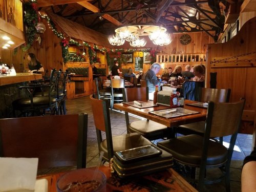Cozy restaurant interior with wooden decor, festive lights, and diners enjoying meals at tables.
