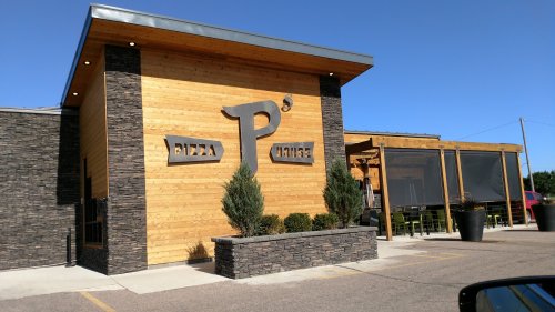 Exterior of a modern pizza restaurant with wooden and stone elements, featuring a large "P's Pizza" sign.