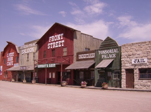 A row of old Western-style buildings, including a saloon, cafe, and jail, under a clear blue sky.