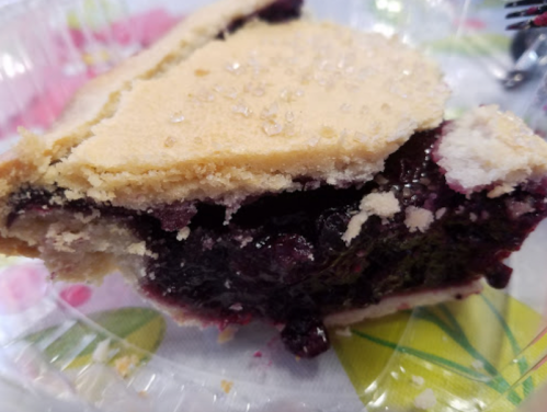 A slice of blueberry pie with a golden crust, revealing dark berry filling and a sprinkle of sugar on top.