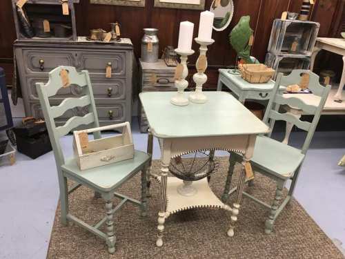 A vintage-style table with two matching chairs, candles, and decorative items in an antique shop setting.