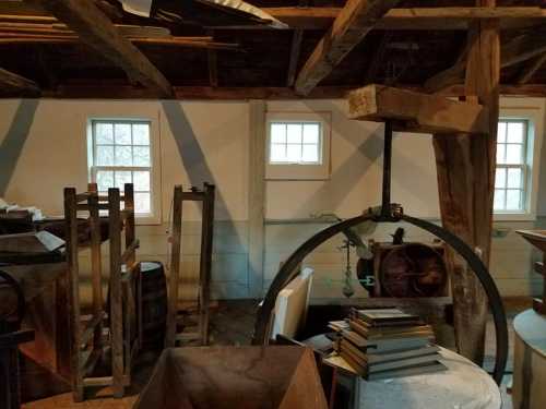 A dimly lit attic space with wooden beams, windows, and various old items like barrels and stacks of books.