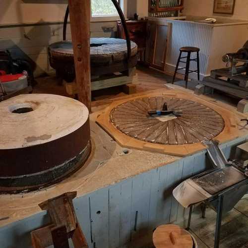 Interior of a workshop featuring large grinding wheels and tools on a wooden floor. Natural light filters in.