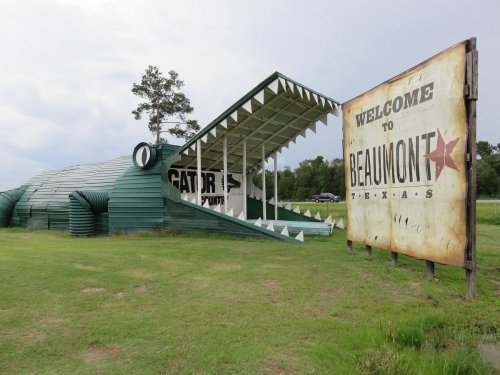 A large alligator-shaped structure next to a "Welcome to Beaumont, Texas" sign, set in a grassy area.