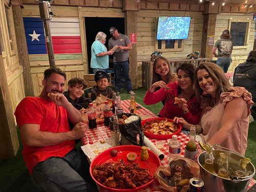 A group of people enjoying a meal of seafood at a rustic setting with a Texas flag in the background.