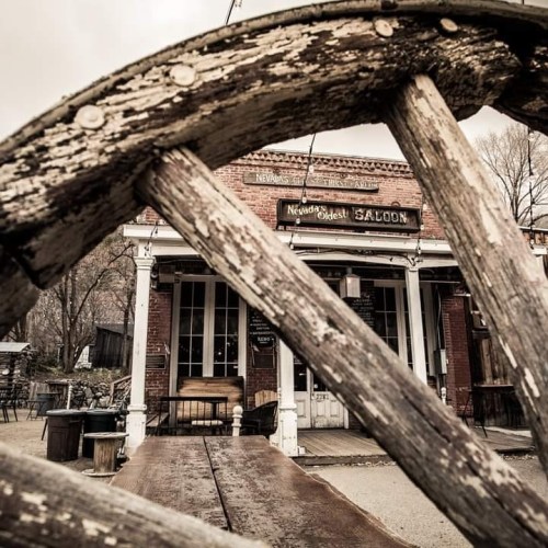 A weathered wooden wheel frames the entrance of Nevada's oldest saloon, showcasing rustic architecture.