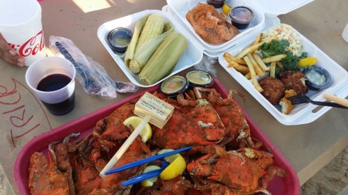 A feast featuring crabs, corn, fries, coleslaw, and drinks on a table covered with brown paper.