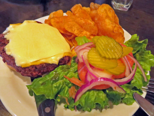 A plate with a cheeseburger topped with melted cheese, served with a side of potato chips and a fresh salad.