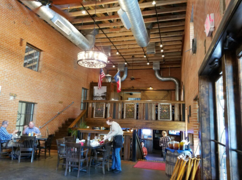 Interior of a rustic restaurant with exposed brick walls, wooden beams, and a chandelier, featuring diners at tables.