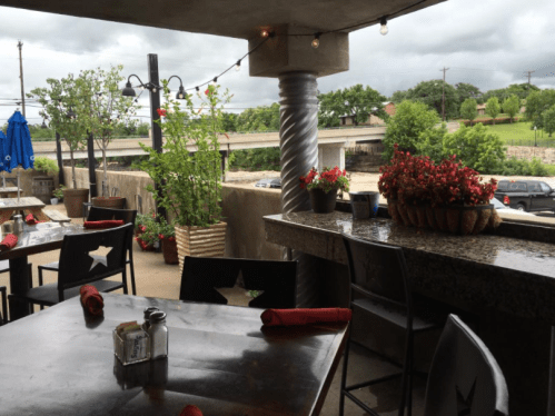 Outdoor dining area with tables, red napkins, and potted plants, overlooking a cloudy landscape and highway.