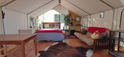 Cozy interior of a glamping tent featuring a bed, sofa, dining table, and rustic decor.