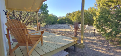 A wooden deck with an Adirondack chair overlooks a serene, wooded landscape.