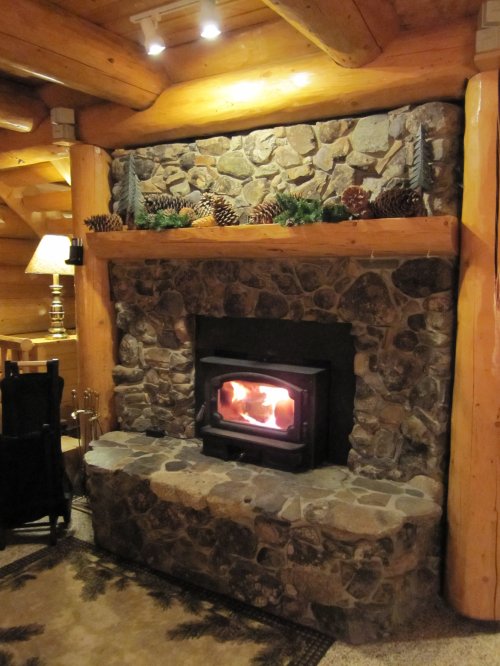Cozy stone fireplace with a wood-burning stove, surrounded by wooden beams and decorated with pinecones and greenery.