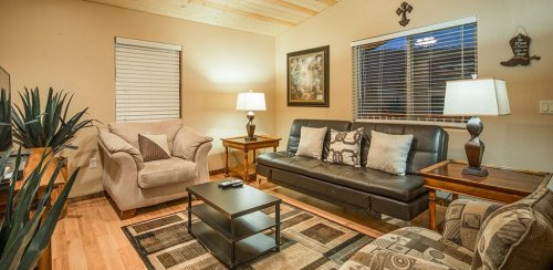 Cozy living room with a sofa, armchair, coffee table, and lamps, featuring warm lighting and wooden accents.