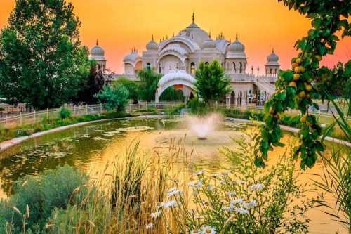 A serene landscape featuring a grand palace at sunset, surrounded by lush greenery and a tranquil pond with a fountain.