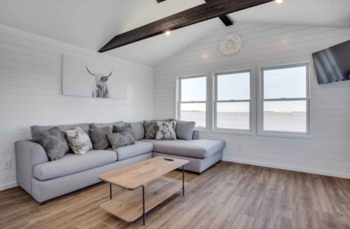 A cozy living room with a gray sectional sofa, wooden coffee table, and large windows overlooking a scenic view.