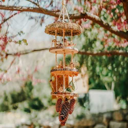 A decorative hanging mobile made of wood and pinecones, surrounded by blooming trees in a serene outdoor setting.