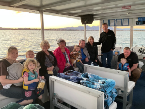 A group of adults and children sitting on a boat, enjoying a scenic view during sunset.