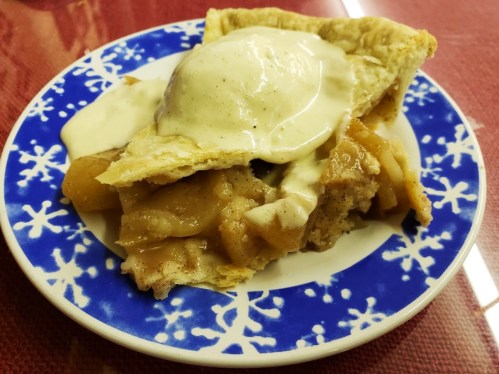 A slice of apple pie topped with vanilla ice cream on a blue and white snowflake-patterned plate.