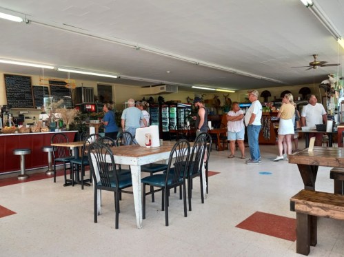 A busy café interior with customers at the counter and tables, featuring a relaxed atmosphere and various food displays.