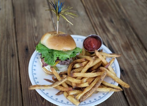 A plate with a burger topped with lettuce and a decorative pick, served with crispy fries and a side of ketchup.
