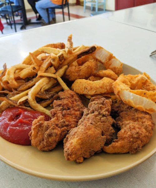 A plate of crispy fried chicken, onion rings, and curly fries, served with a side of ketchup.