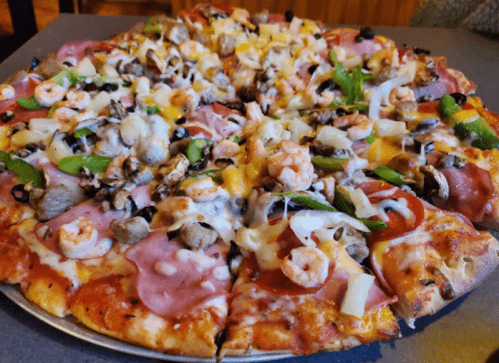 A large pizza topped with shrimp, ham, green peppers, mushrooms, olives, and cheese on a golden crust.