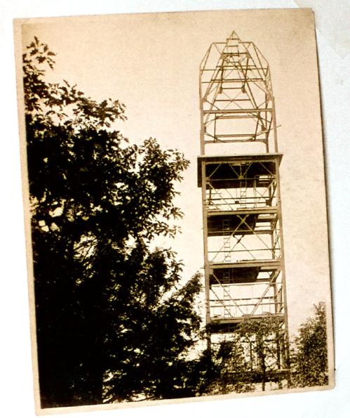 Black and white photo of a tall, partially constructed tower surrounded by trees.