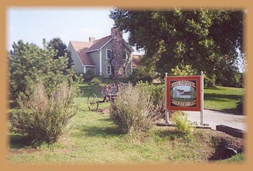 A quaint house with a stone chimney, surrounded by greenery and a sign for "Big Grove" in the foreground.