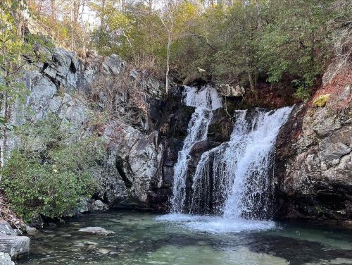 A serene waterfall cascading over rocks into a clear pool, surrounded by lush greenery and autumn foliage.