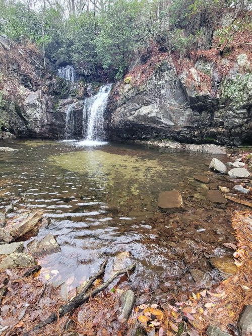 A serene waterfall cascades into a calm pool, surrounded by rocky terrain and lush greenery.