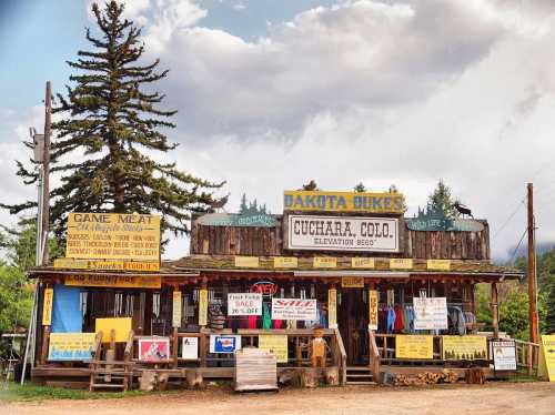 A rustic storefront with signs for game meat and outdoor gear, surrounded by trees under a cloudy sky.