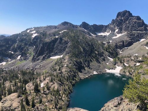 A scenic mountain landscape featuring a clear blue lake surrounded by rocky terrain and green trees under a blue sky.