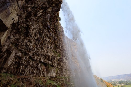 A waterfall cascading over a rocky cliff, with mist rising into the air against a clear sky.