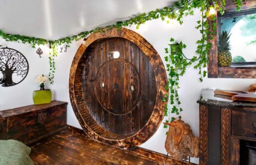 A cozy room featuring a circular wooden door, ivy decor, and rustic furnishings, creating a whimsical atmosphere.