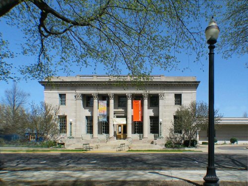 Historic building with columns, banners, and trees in front, set against a clear blue sky.