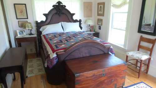 Cozy bedroom featuring a wooden bed with a quilt, a trunk at the foot, and natural light from a window.