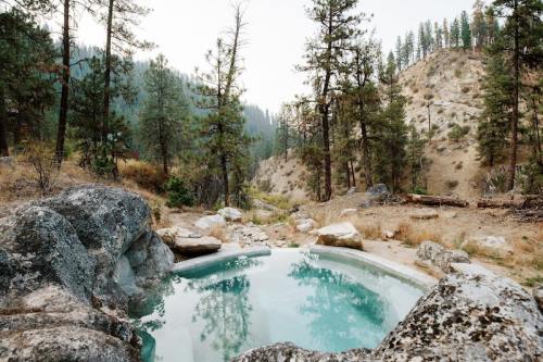 A serene hot spring surrounded by rocky terrain and tall pine trees in a mountainous landscape.