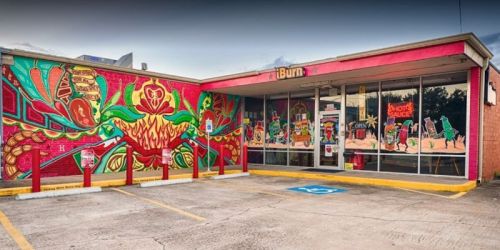 Colorful mural on a restaurant exterior featuring vibrant designs and a welcoming entrance with parking spaces.