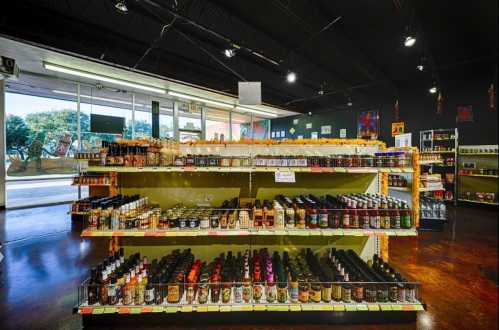 A well-stocked shelf in a store displaying various bottles of sauces and condiments under bright lighting.