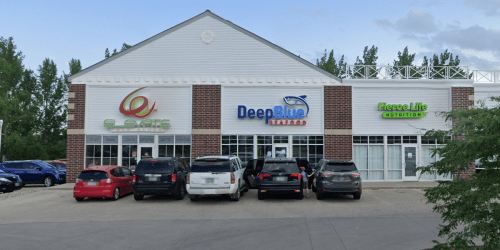 A storefront featuring three businesses: Glaze, DeepBlue, and Emerge Life Nutrition, with parked cars in front.